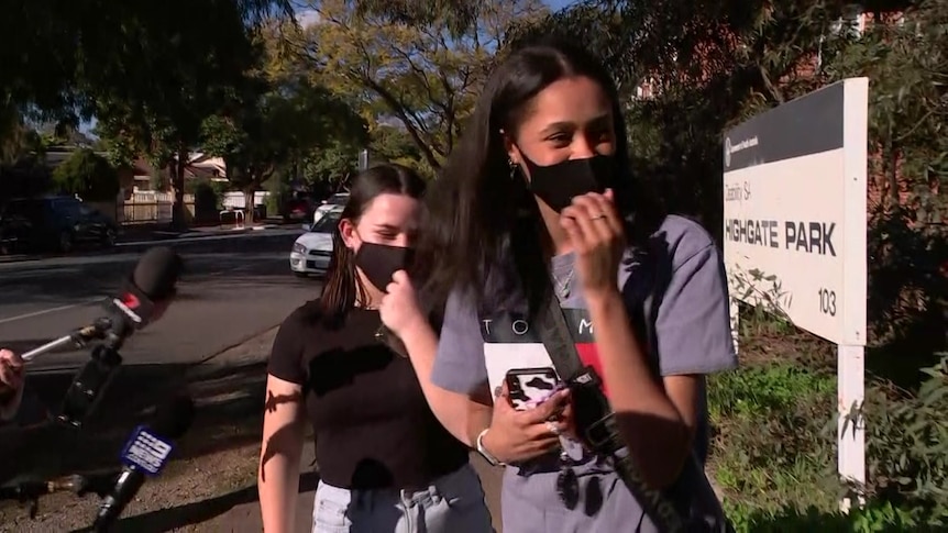 Two young women wearing masks outside a sign saying Highgate Park