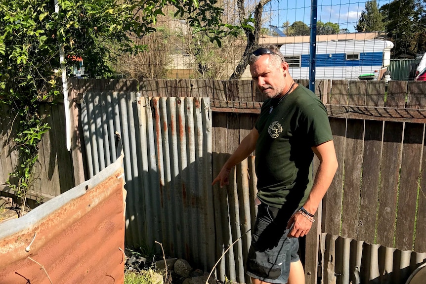 Justin Brow pointing out areas of his fence that have been reinforced with wire, corrugated iron and concrete.
