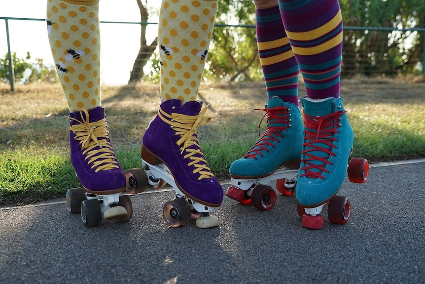A close-up photo of two women wearing multi-coloured socks and wearing rollerblades.