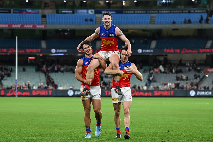 Lachie Neale carried off the AFL field by two teammates, celebrating a milestone