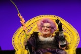 Australian performer Barry Humphries as his alter ego Dame Edna Everage holding a peach coloured gladioli flower