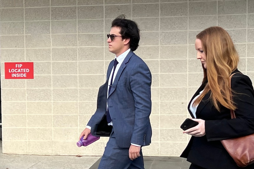 A man in a grey suit and sunglasses walking out of the ACT court. 
