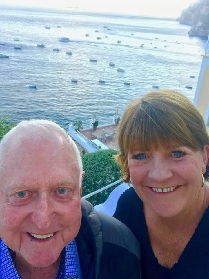 A man and a woman smiling into the camera in front of the ocean.