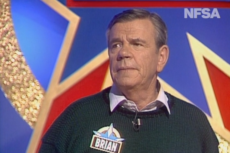 A man in a sweater in a game show setting 