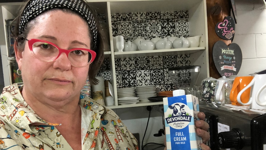 Woman holds up bottle of long life milk in her cafe.