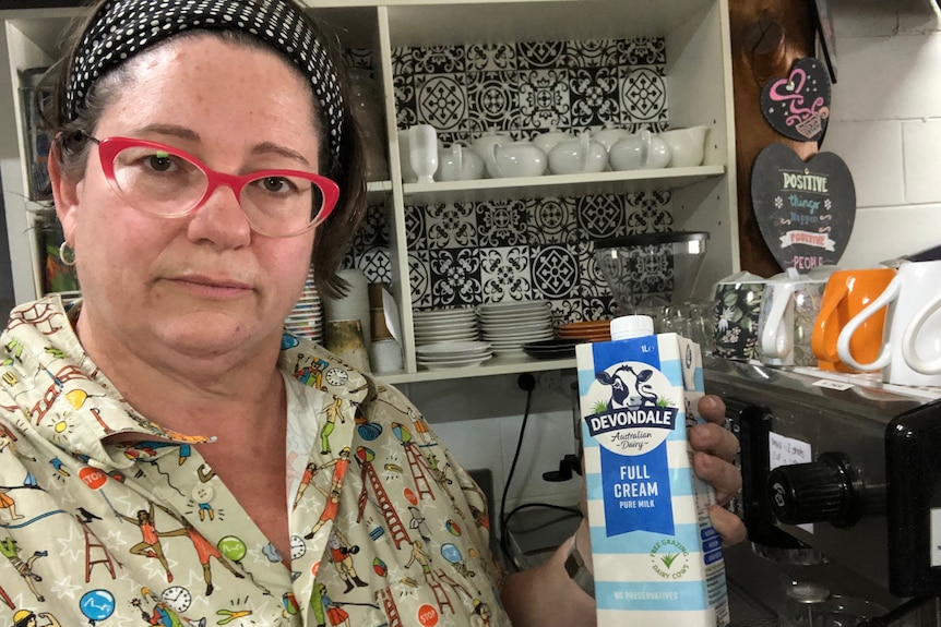 Woman holds up bottle of long life milk in her cafe.