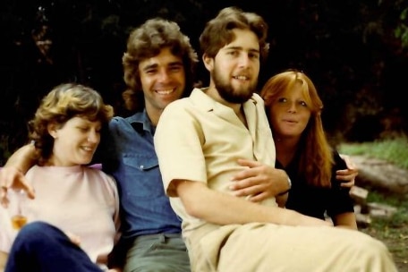 An old photograph of four young people, two women and two men smiling with arms around one another.