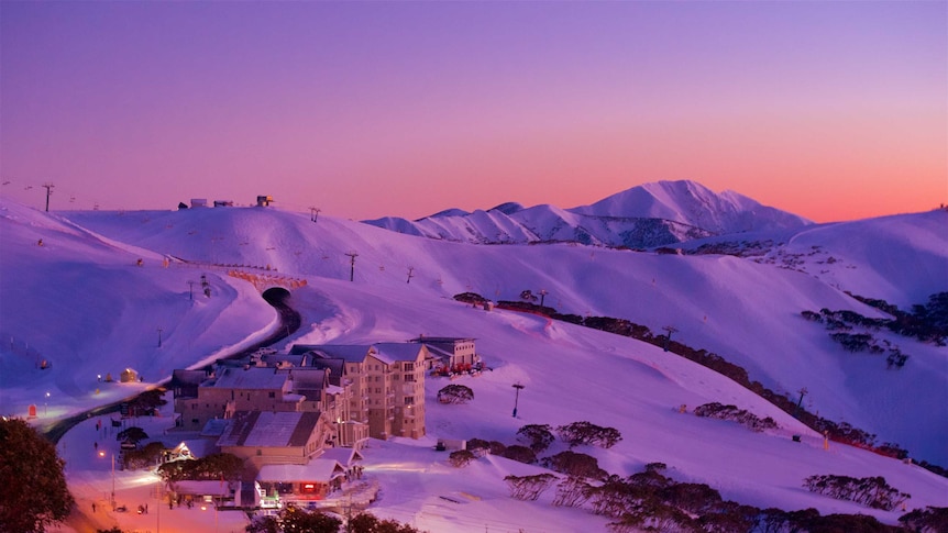 Sunset over a mountainous, snow-covered resort in Victoria, with several buildings and many trees.