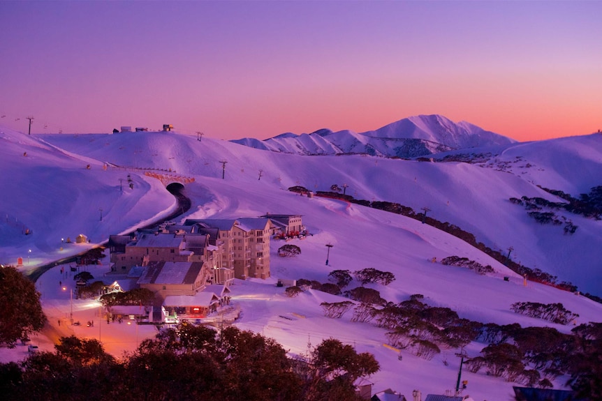 Sunset over a mountainous, snow-covered resort in Victoria, with several buildings and many trees.