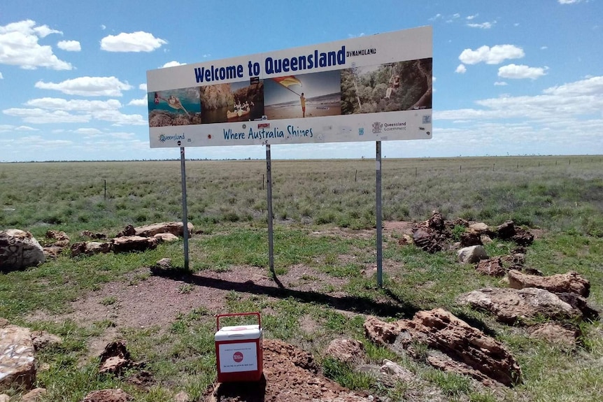 A photo of the red esky in front of a 'Welcome to Queensland' sign at the state's border.