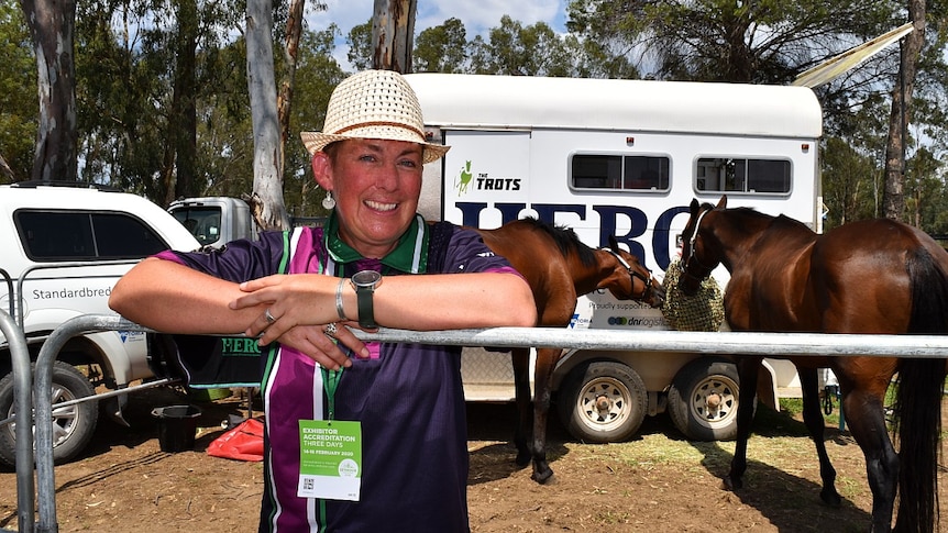 A woman stands in front of horses feeding.