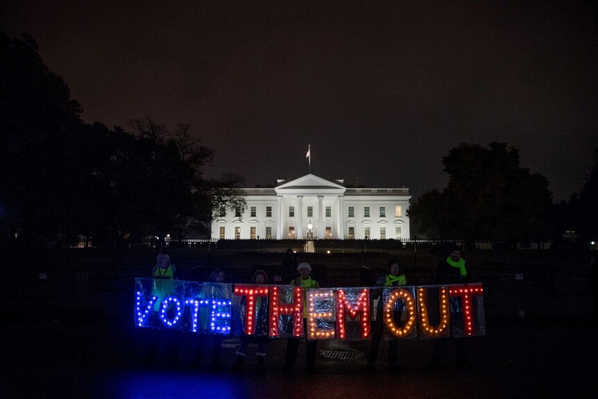 A group of people hold up a sign that reads "Vote Them Out" as they protest in front of the White House.