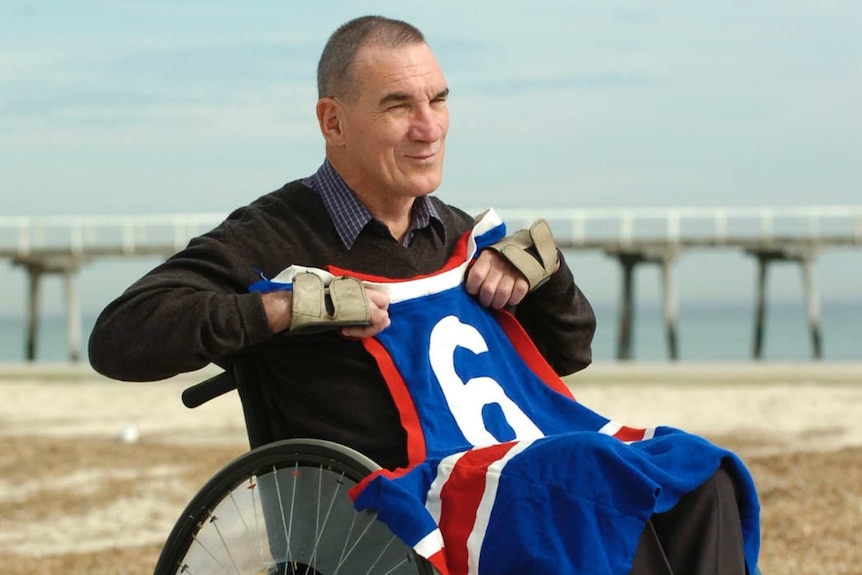 Former footballer Neil Sachse holds his Footscray jumper while sitting in a wheelchair.