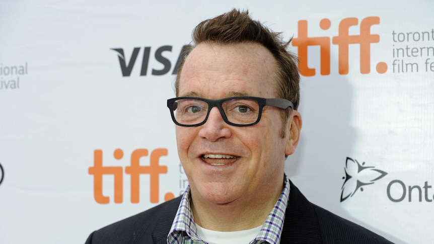 Tom Arnold smiles in a suit