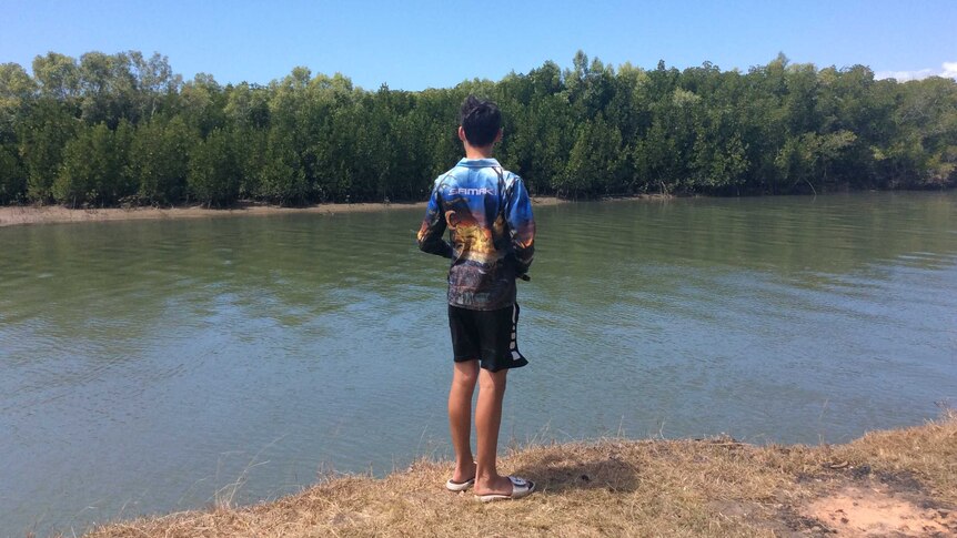 Boy casting a fishing line on the banks of a bay.