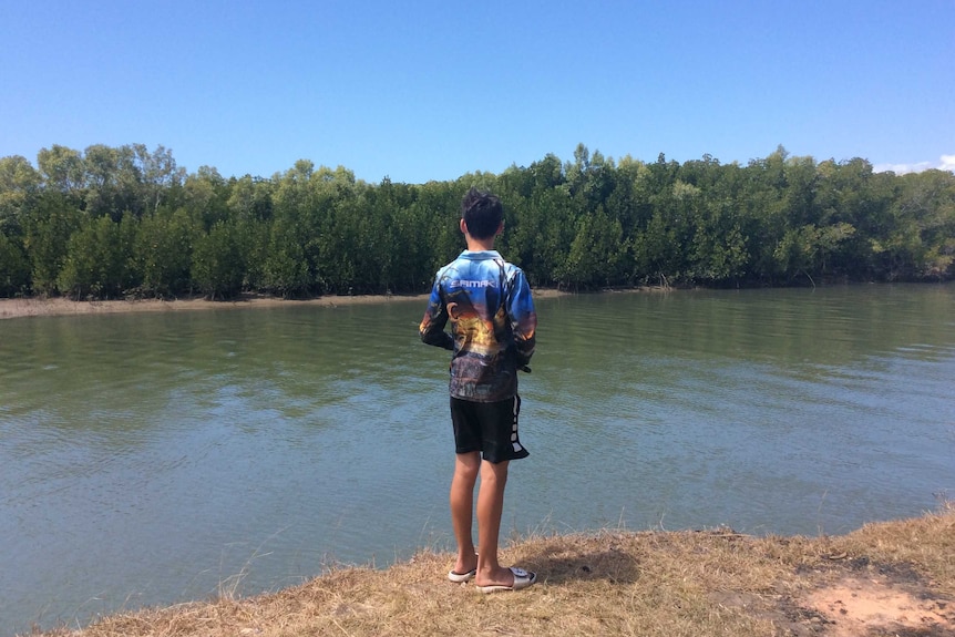 Boy casting a fishing line on banks of a bay.