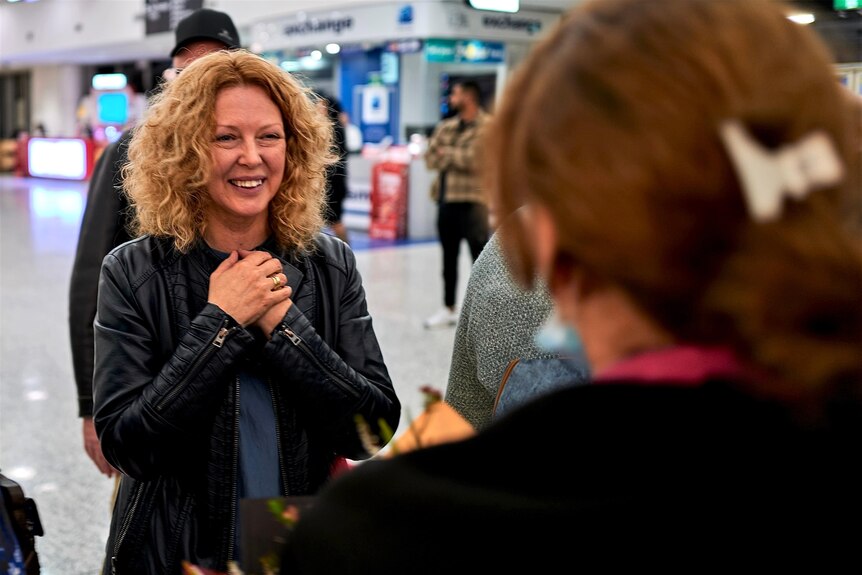 a woman smiling as she greets another woman at the airport