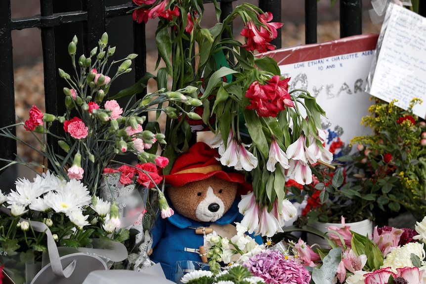 A stuffed Paddington Bear is pictured, surrounded by flowers and cards.
