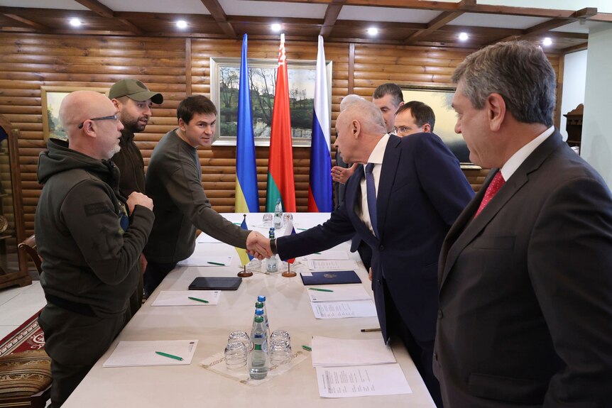 Ukrainian and Russian delegates shake hands across table.