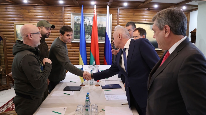 Ukrainian and Russian delegates shake hands across table.