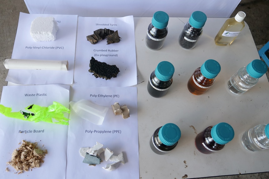 Eight different types of solid waste next to nine jars of oil and fuel layed out on a table. 