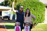 A father and mother stand in driveway with two girls dressed up in sunglasses and tiara.