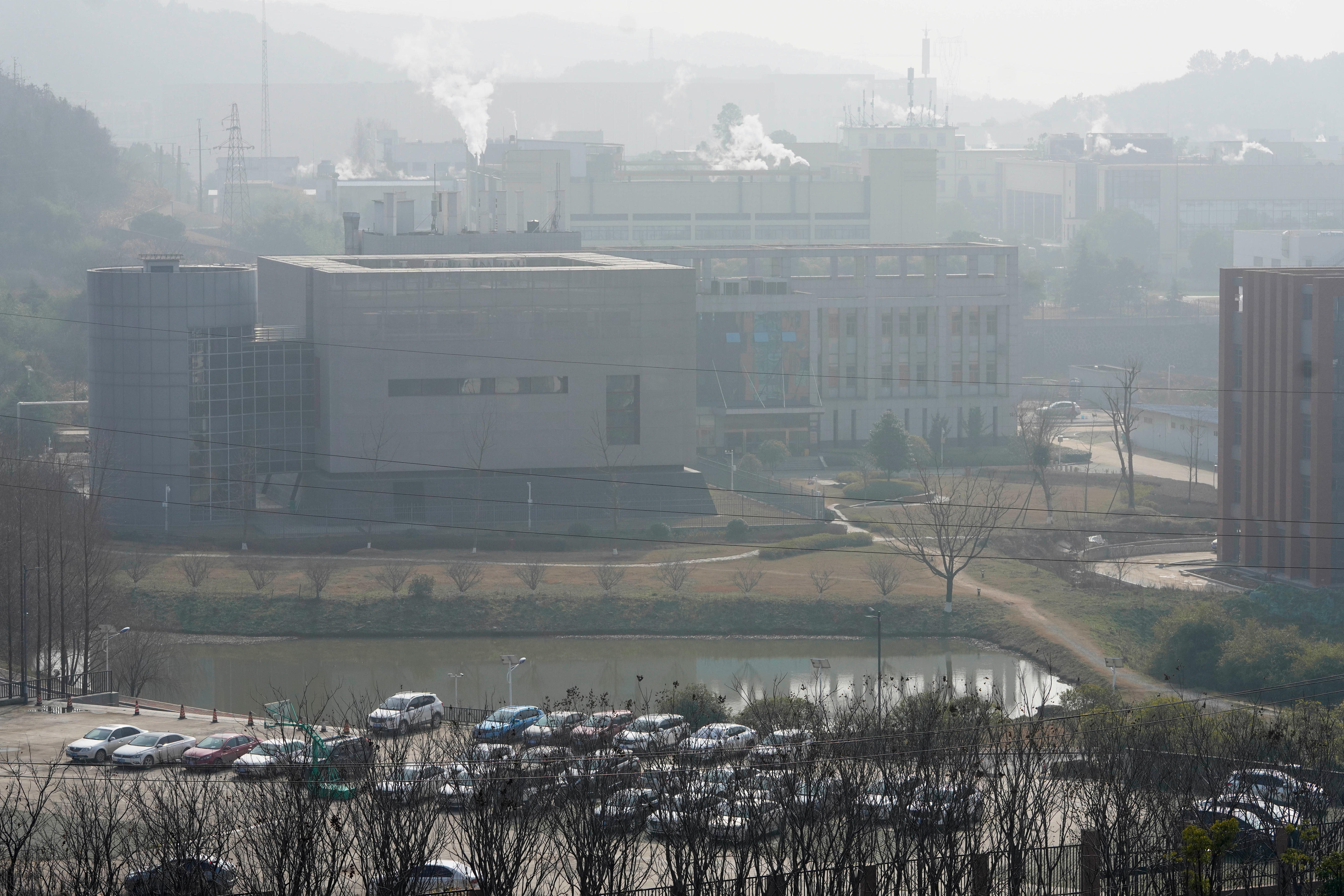 An exterior shot of a building surrounded by other buildings, smoke billowing from vents and a hazy sky 