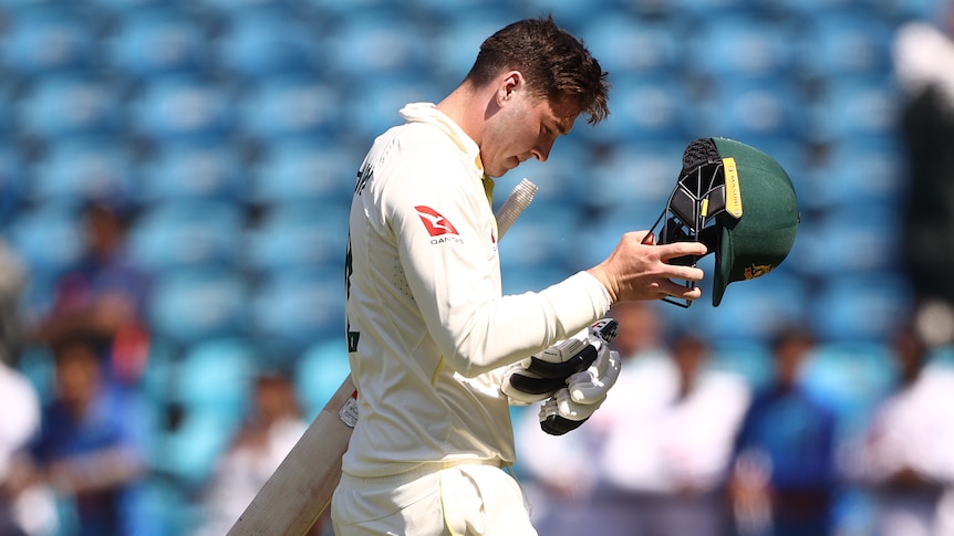 A cricket player in whites walks off, removing his helmet.