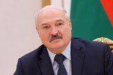 Alexander Lukashenko sits at a desk with microphones. Behind him is the Belarusian flag.