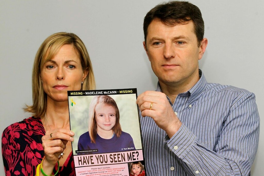 A blonde woman and brown haired man hold up an image of a young girl.