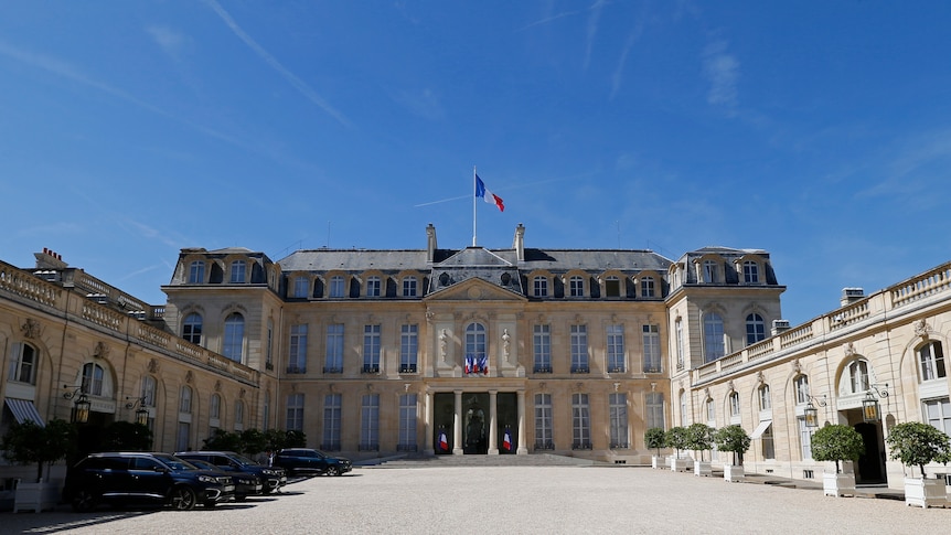 a wide shot of the courtyard of the Elysee Palace at day time with the french flag on the roof