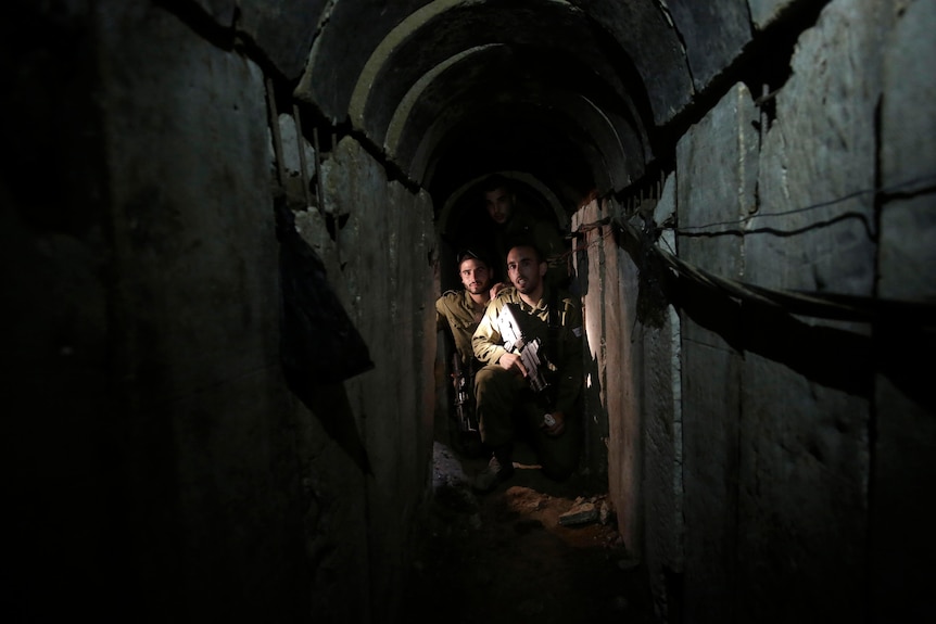 Two Israeli soldiers squat inside an undergorund tunnel.