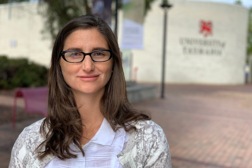 A woman with brown hair and glasses stares at the camera