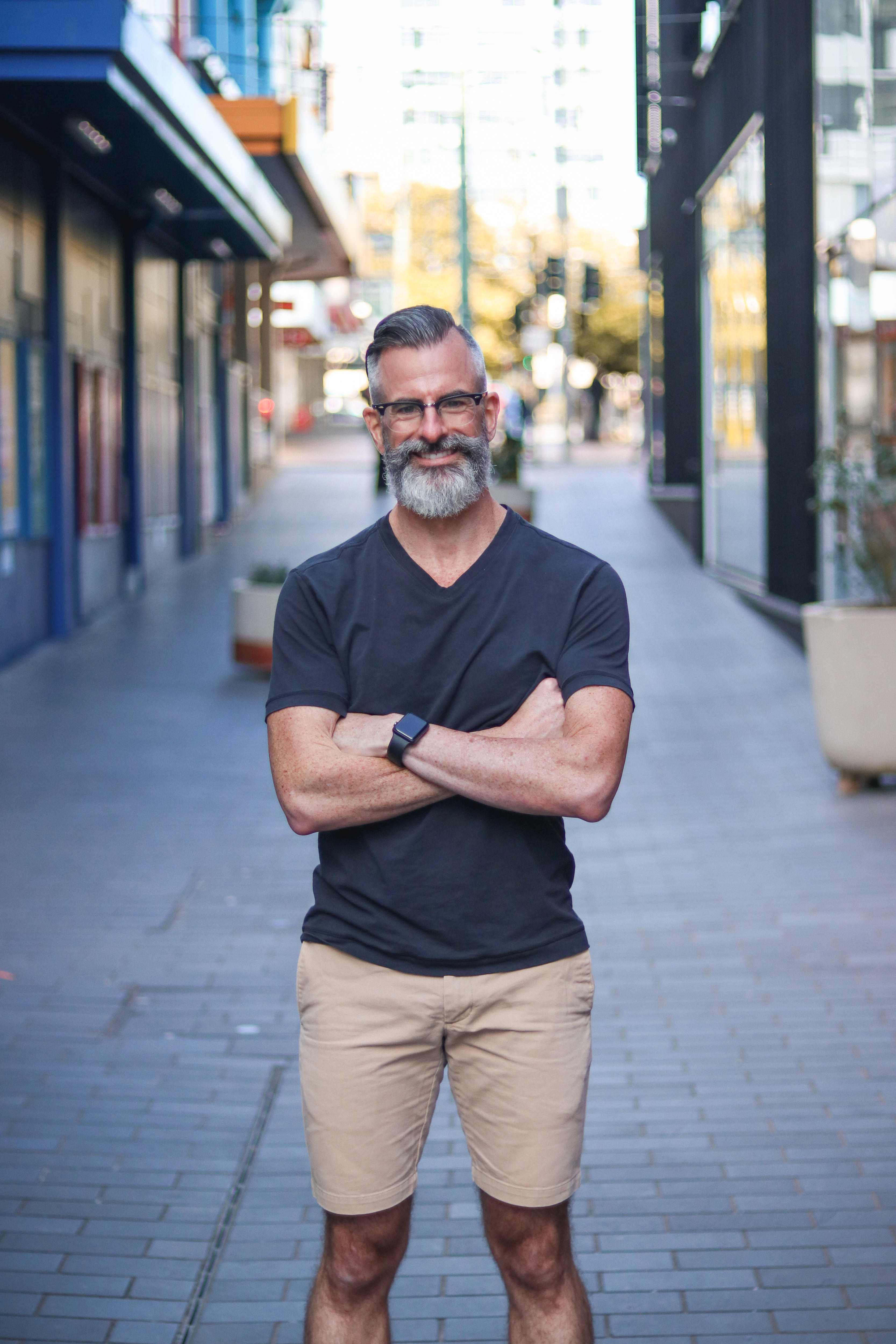 A man with grey hair and a beard stands in a street