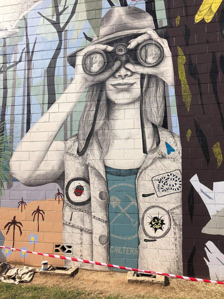 Black and white figure of a young girl holding binoculars up to her face painted over a brick wall