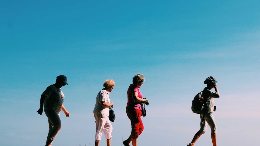 Four middle-aged women carrying cameras and backpacks walk in a line.