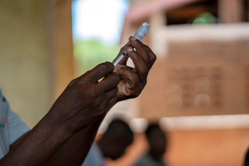 A close-up of an African man's hands drawing a needle from a small vial of vaccine.