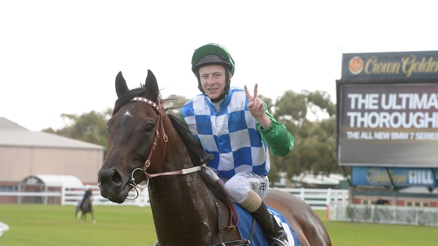Jockey Harry Coffey sitting atop Signoff, giving the peace symbol with his fingers.