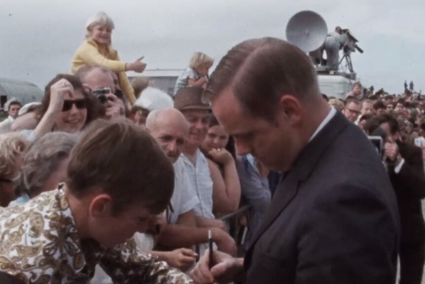 Neil Armstrong writes on the hand of a young boy in a crowd of people.