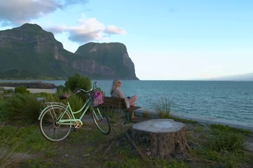 Lady sits on a public seat near the ocean on Lord Howe Island illustrating our Gardening Australia episode recap.