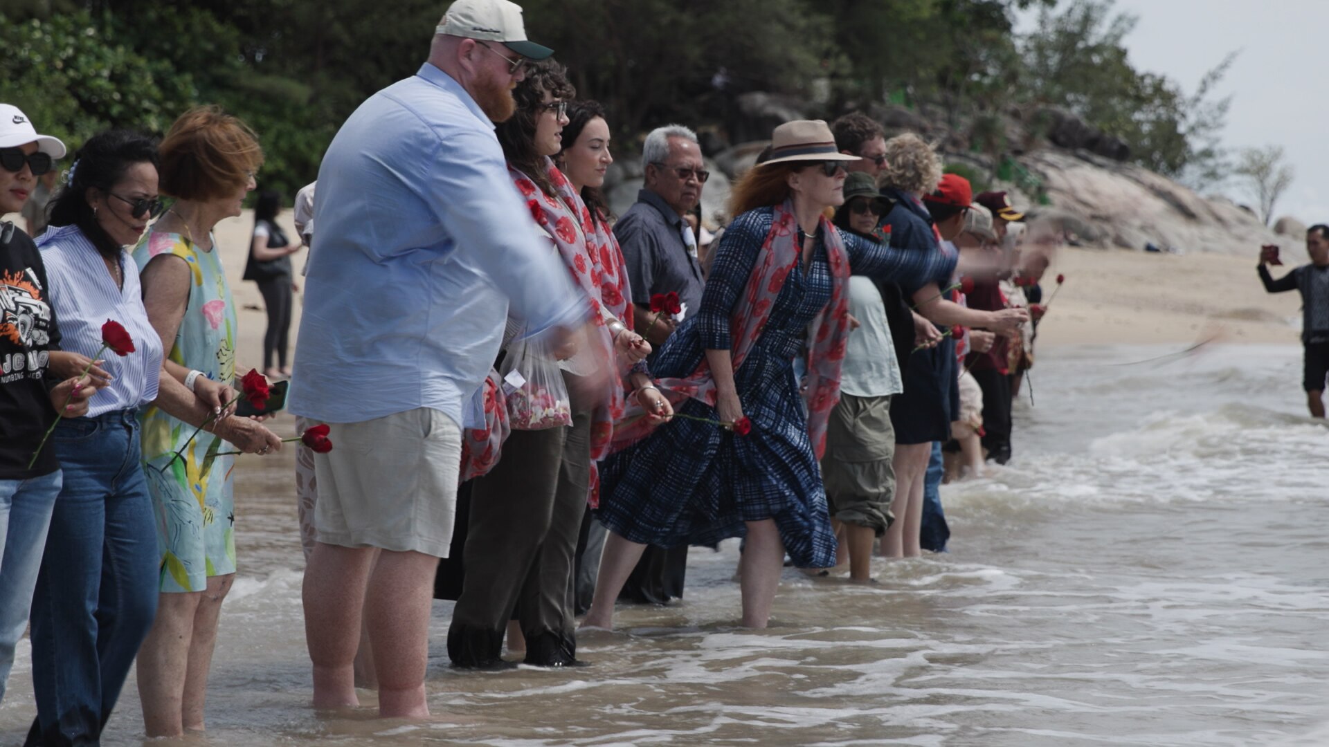 Line of people in shallows throw flowers into the sea