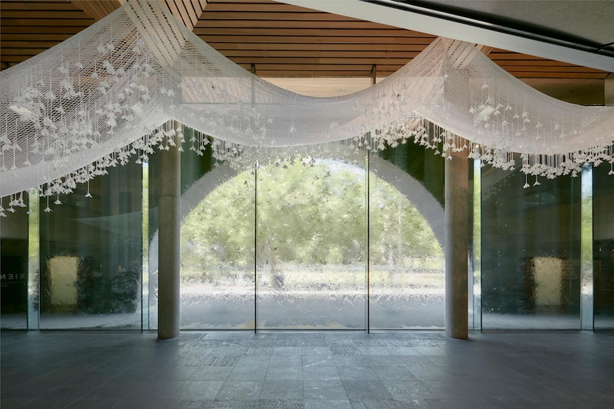 A vast white net suspended from the ceiling with large windows in the background.