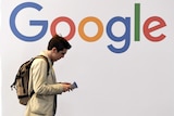 A man walks past a multi-coloured logo spelling Google