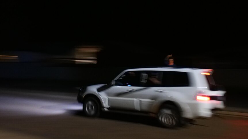 a white 4WD travels down a road at night as a small child hangs out the window