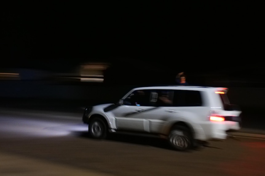 a white 4WD travels down a road at night as a small child hangs out the window