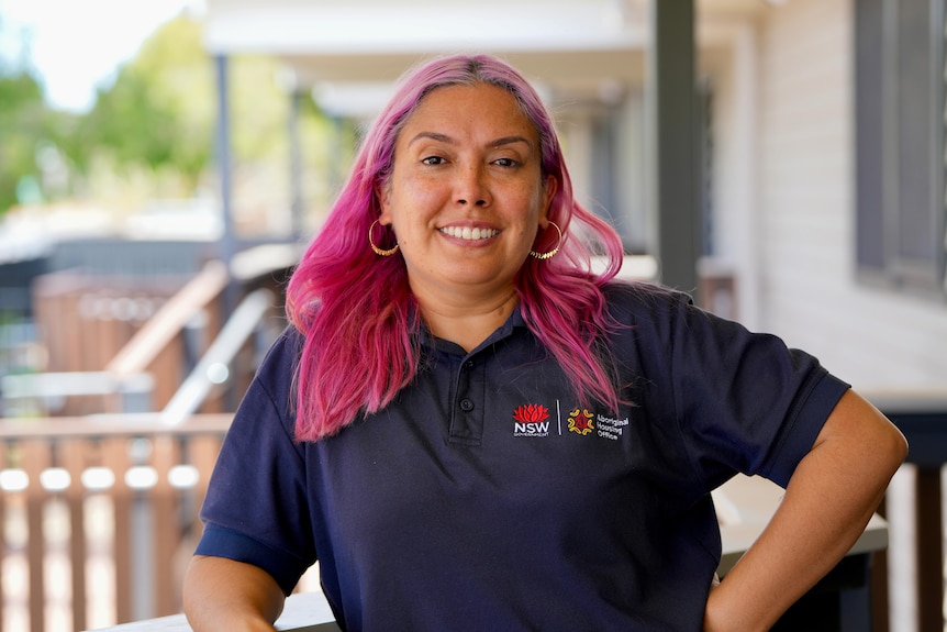 An aboriginal woman with purple hair wearing a black tshirt posing for a photo. 