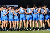A group of men wearing football uniforms huddle together on oval. 