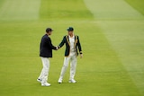 Two cricketers shake hands in a green field