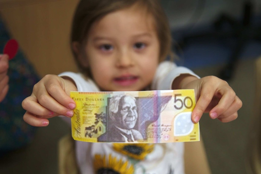 A kindergarten-aged child holds a pretend $50 note in front of her.