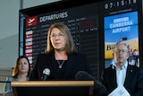Catherine King stands at lecturn in front of airport signage